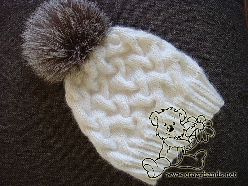 winter cable hat made with white yarn and decorated with silver fox fur pom pom