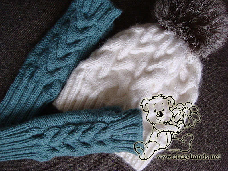 a pair of cable knit fingerless gloves next to a knit winter hat with fur pom pom