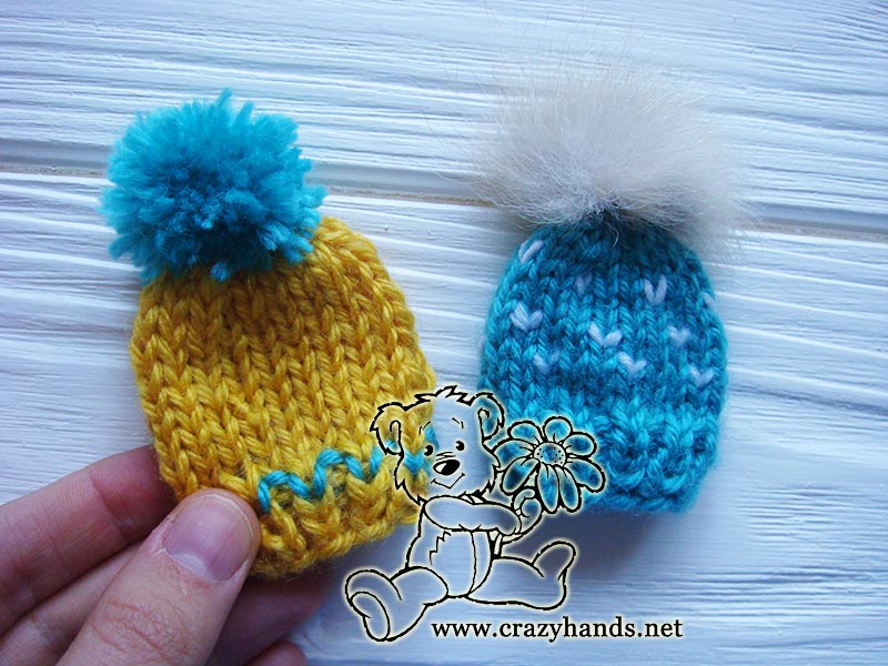two knit mini hats - one yellow with yarn pom and one blue with fur pom