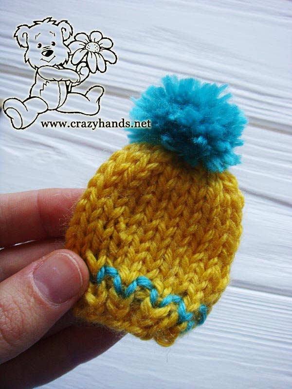knit yellow mini hat with blue yarn pom pom
