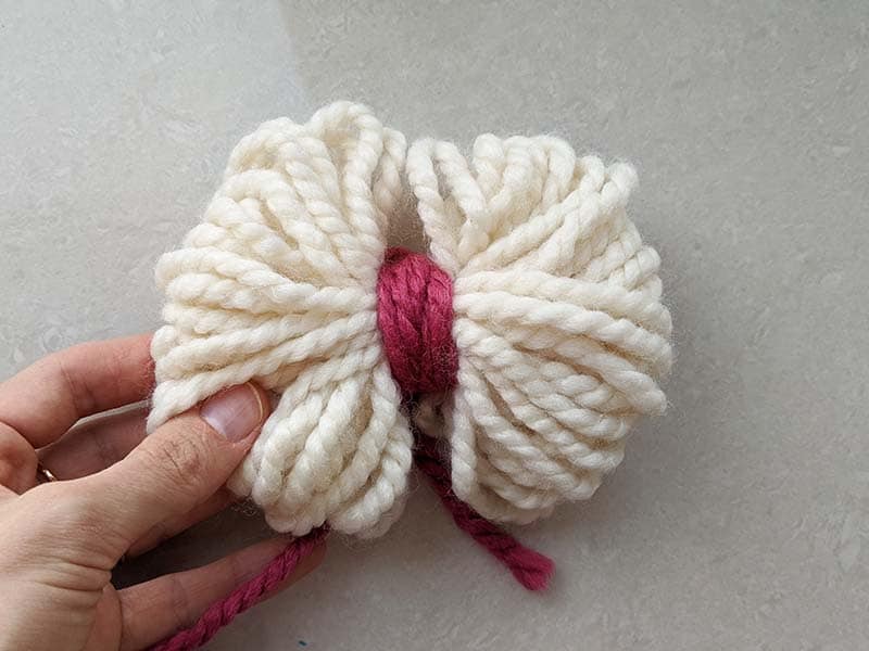 how to make a bow from the yarn. step two - use a piece of yarn to tighten bunch of yarn in the middle