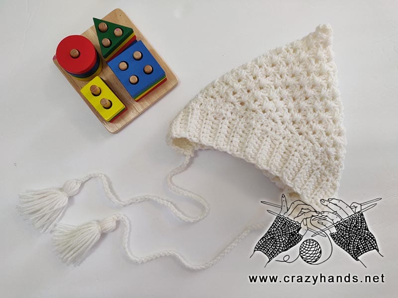 crochet white pixie hat for babies is shot next to a puzzle toy