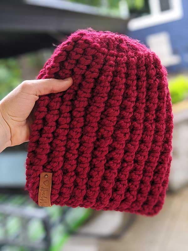 finished bubble ribbed knit hat made with dark red yarn is held in the hand with blurred background