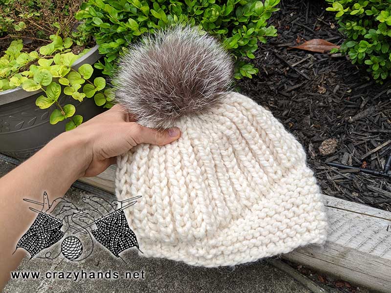 crown jewel chunky knit hat with fur pom pom held in hand