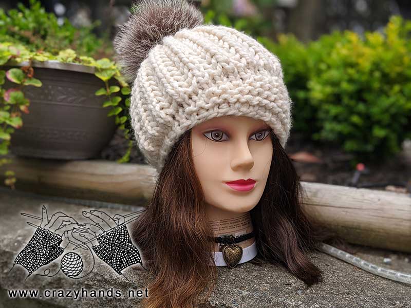 crown jewel chunky knit hat with fur pom pom on the mannequin's head - front view