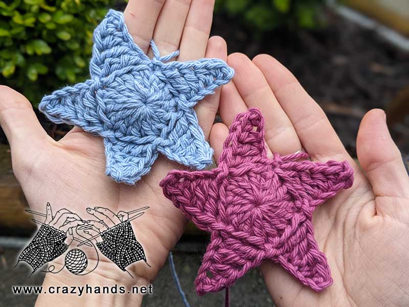 two five point crochet stars on the hands - one is blue and another one is violet