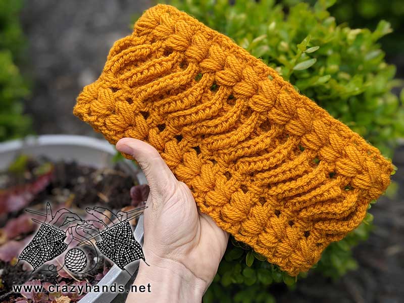 crochet lace ear warmer held in the hand with a greenery on the background