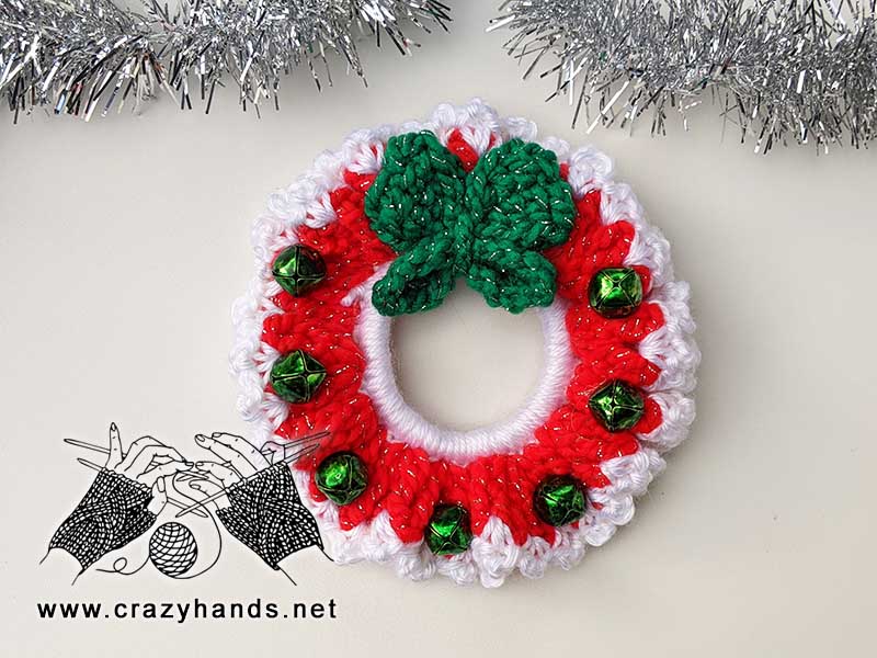 crochet christmas wreath with red base, white edge, butterfly at the top and bells along the edge