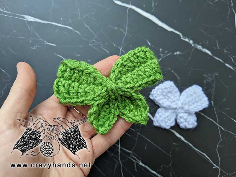 two crochet bow butterflies (green and white) shot on a marble background