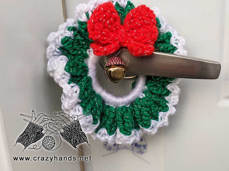 crochet green christmas wreath with red butterfly on the door handle