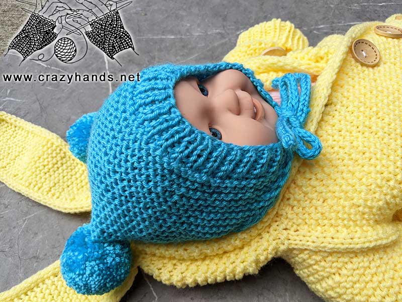 baby doll wears blue bonnet inside yellow knit baby cocoon