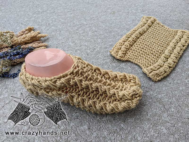 two (2) needles popcorn knit socks - one finished sock is fit on the mannequin's foot and the one is laying flat on the ground
