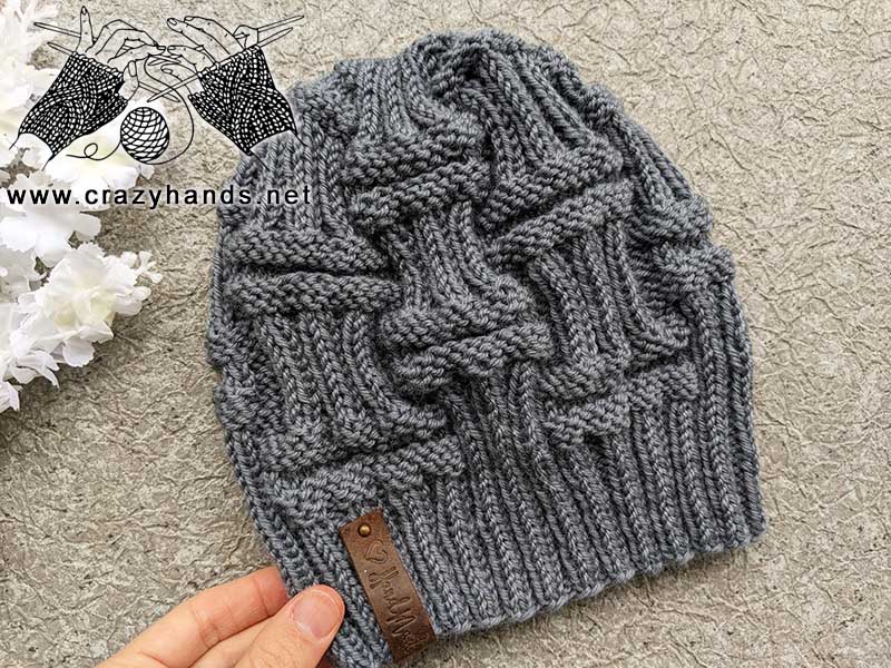gray color knit pillar hat made for men shot on a flat surface next to a white flower