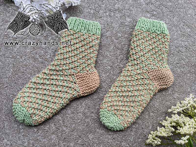 a pair of flat knit socks made with green and brown yarn shot on a flat surface