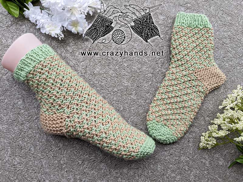 a pair of knit flat two-color socks. One is shown on a mannequin foot and the other one on the flat surface.