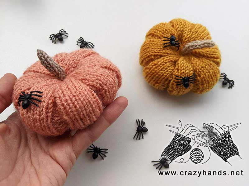 two knit haloween pumpkins, one light pink and another one light brown, with a bunch of decor spider on the pumpkins and around them